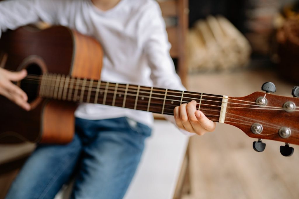 A close-up of a child practicing guitar chords indoors, emphasizing hands and strings.