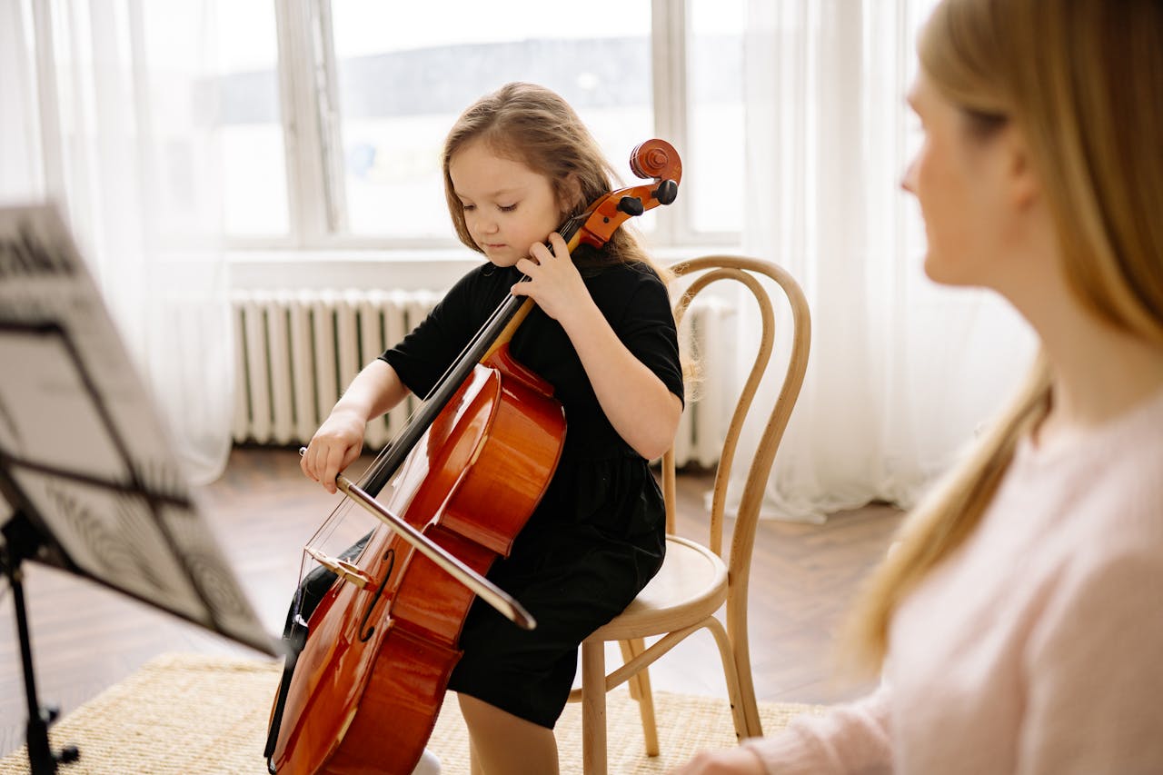 A young girl playing the cello during a music lesson at home with her teacher.